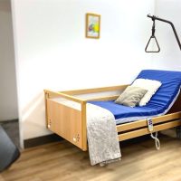 3 funkciós wissner-bosserhoff elektromos ápolási ágy, emelt háttámlával, kapaszkodóval és fa éjjeliszekrénnyel.