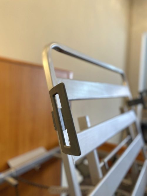 Közelkép egy Stiegelmeyer ágy háttámla-emelő mechanizmusáról, fém rácsos szerkezettel és állítható fogantyúval.