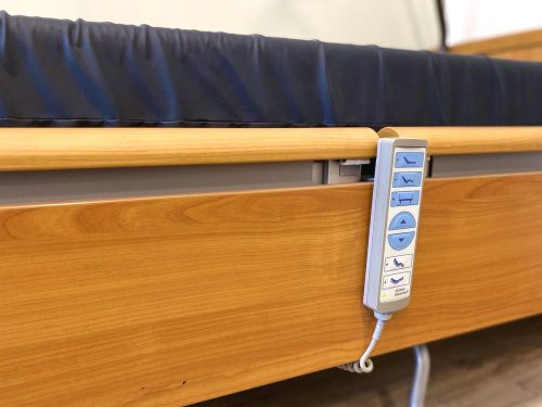 Elektromos betegágy vezérlője felfüggesztve az ágy oldalán, fa borítással