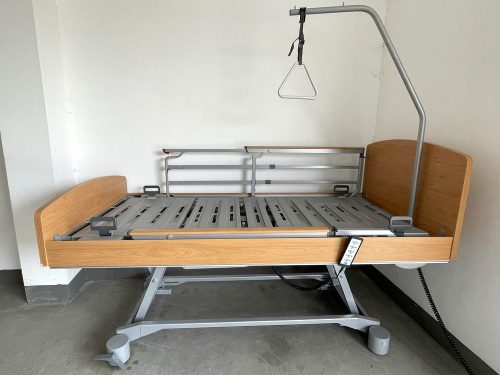 Az elektromos betegágy teljesen felemelt állapotban látható, teleszkópos biztonsági korlátokkal, állítható kapaszkodóval és masszív fém szerkezettel a stabilitás érdekében.