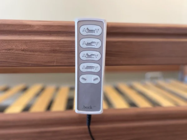 Elektromos betegágy távirányító közelről, háttérben lamellás fekvőfelület