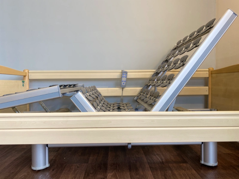 Használt elektromos ápolási ágy oldalnézetből, távirányítóval és állítható korláttal.